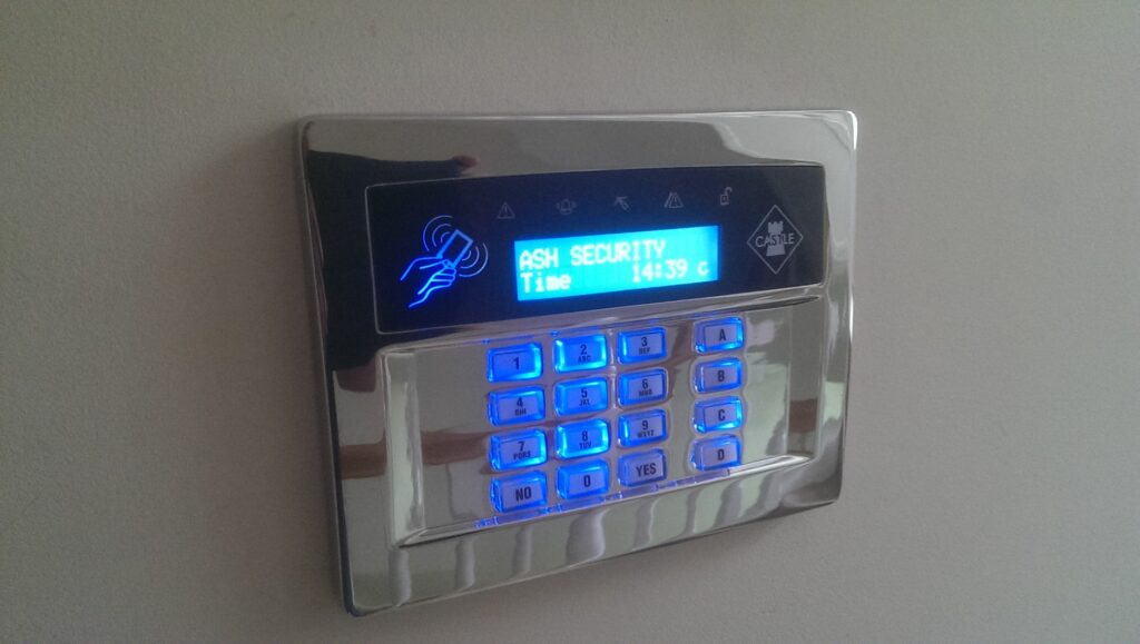 ASH Security keypad with illuminated blue buttons and digital display, showing time and brand name, relevant to professional security installations.