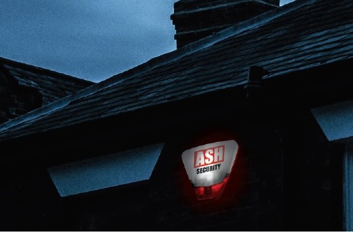 ASH Security alarm light mounted on a house, illuminated in red against a dark evening sky, emphasizing home security solutions during Halloween.