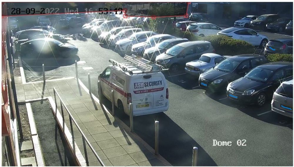 Security camera footage showing ASH Security vehicle parked in a car dealership, surrounded by various cars, with timestamp and monitoring details visible.