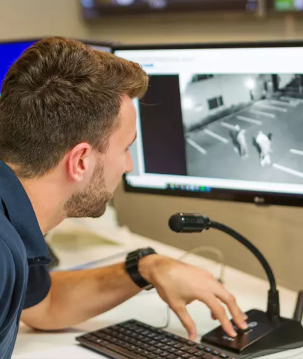 Man monitoring CCTV footage on computer screen, observing potential security threats in a parking lot.